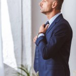 Side view of handsome man in formal wear wearing necktie and looking away at home