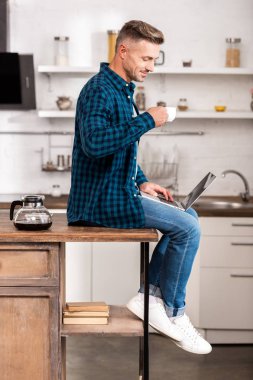 kahve tutarak ve dizüstü evde kullanma kareli gömlek gülümseyen adam yan görünüm
