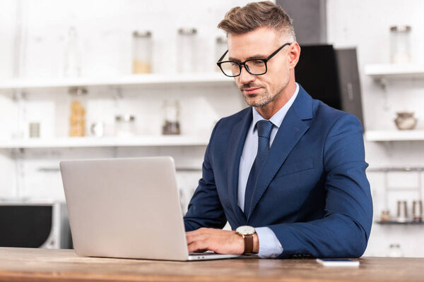 handsome businessman in eyeglasses using laptop at home