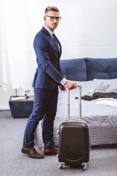 Businessman Suit Eyeglasses Holding Suitcase Looking Camera Bedroom — Stock Photo, Image