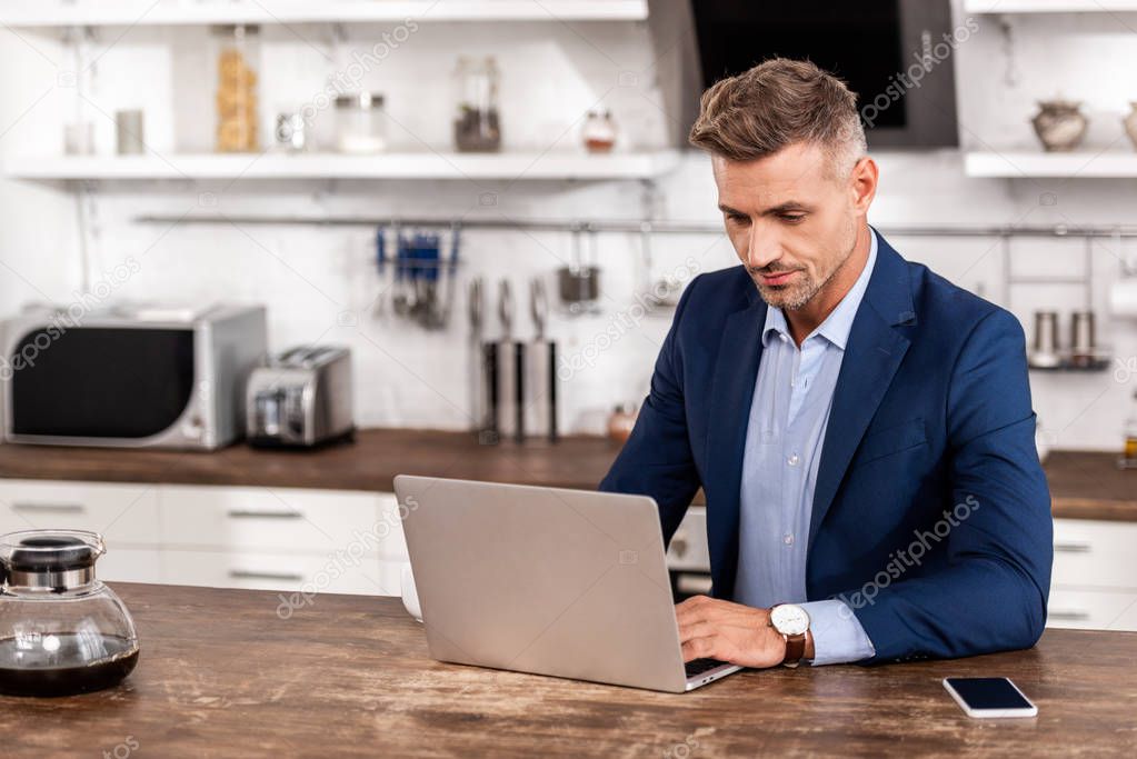 Handsome businessman in formal wear using laptop at home