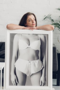 thoughtful transgender woman holding black and white photo with female body in underwear at home clipart