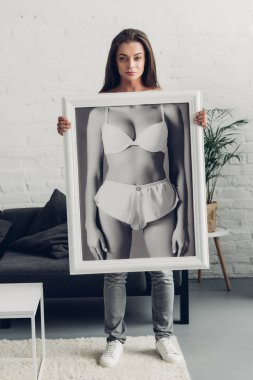 ciddi bir travesti kadın elinde siyah beyaz bir fotoğraf ve evde iç çamaşırlı bir kadın var.