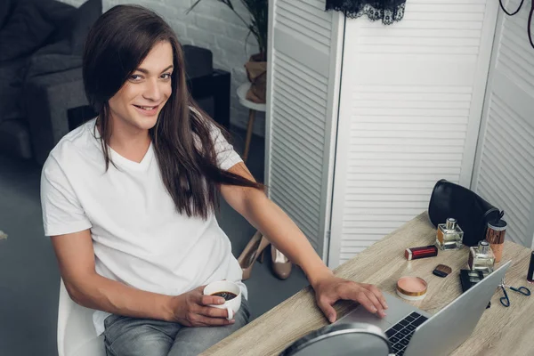 若いトランスジェンダーのフリーランスの女性を笑顔にしながら家でコーヒーを飲みながらカメラを見て — ストック写真