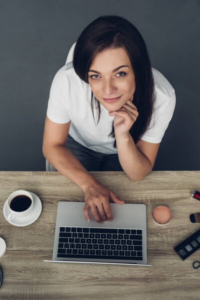 top view of young transgender freelancer woman with cup of coffee sitting at workplace at home