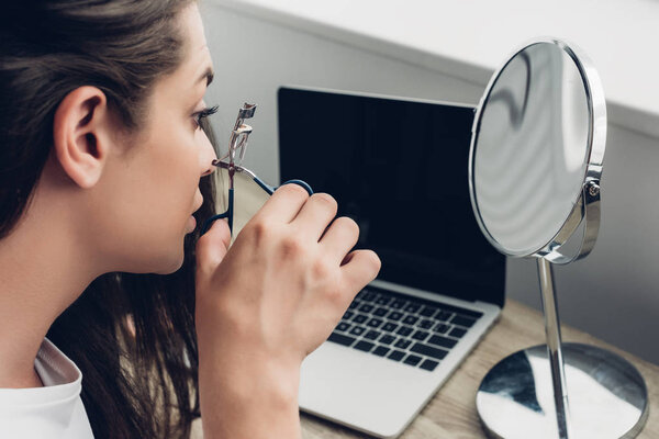 close-up portrait of young transgender woman doing makeup with lash curler at home