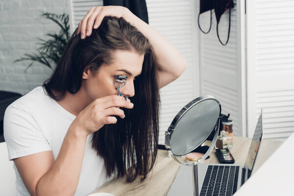 young transgender woman doing makeup with lash curler at home