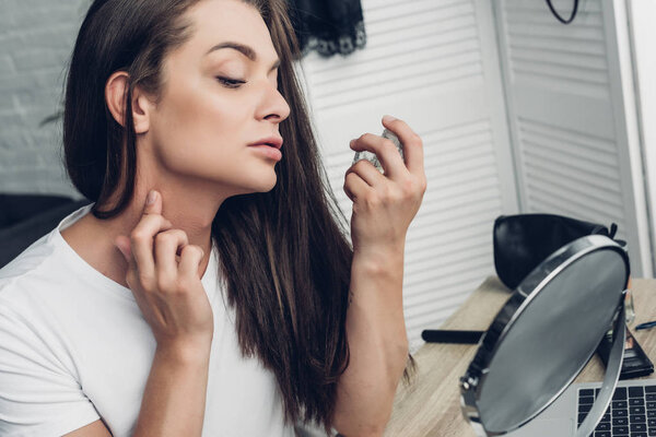 young transgender woman applying perfume on neck at home