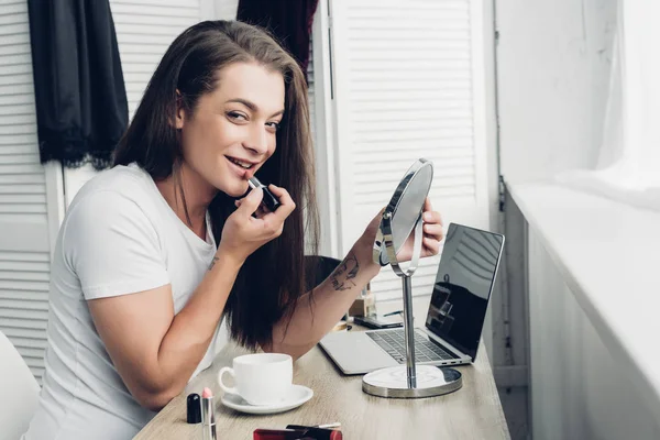 Uśmiechnięta Młoda Transseksualistka Okrągłym Lustrem Makijażu Szminką Patrząc Kamerę — Zdjęcie stockowe