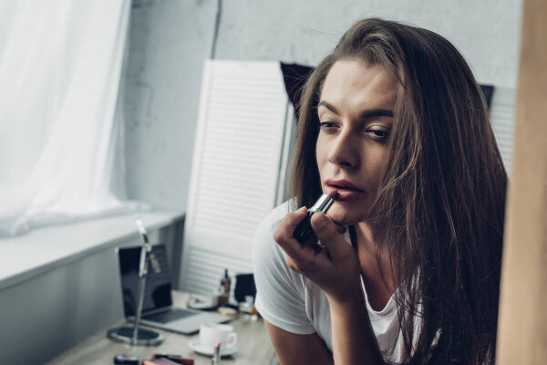 close-up portrait of young transgender woman applying lipstick at home