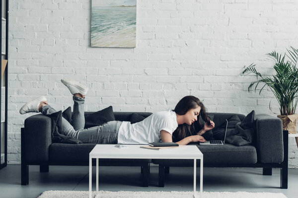 side view of young transgender freelancer woman working with laptop on couch at home