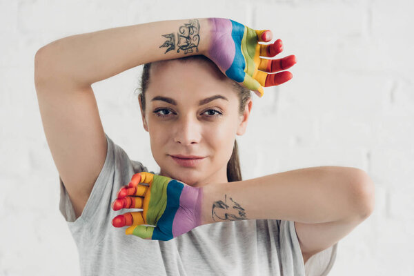 young transgender woman with hands painted in colors of pride flag in front of white brick wall