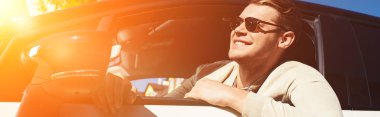 smiling young man leaning out car window of driving automobile clipart