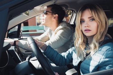 shocked woman at drivers seat looking at camera with boyfriend near by in car clipart