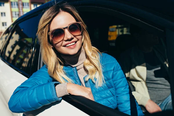 Χαμογελαστό Γυναίκα Γυαλιά Ηλίου Κοιτάζοντας Από Παράθυρο Του Αυτοκινήτου Ενώ — Φωτογραφία Αρχείου