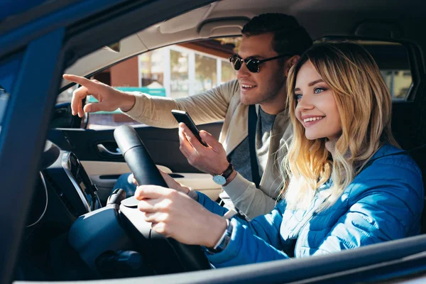 Lächelnder Mann Mit Smartphone Zeigt Freundin Richtung Auto — Stockfoto