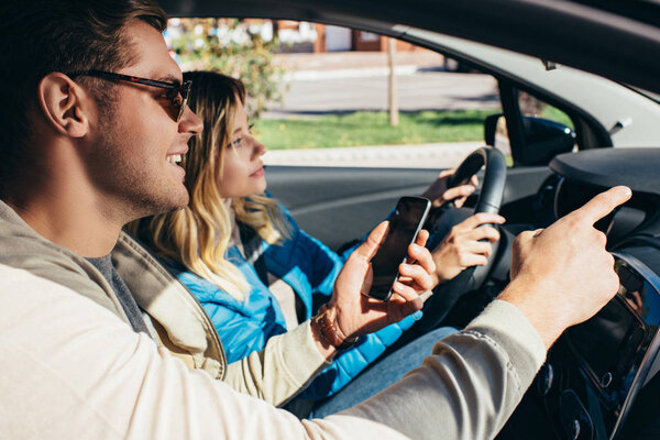 smiling man with smartphone showing direction to girlfriend that driving car