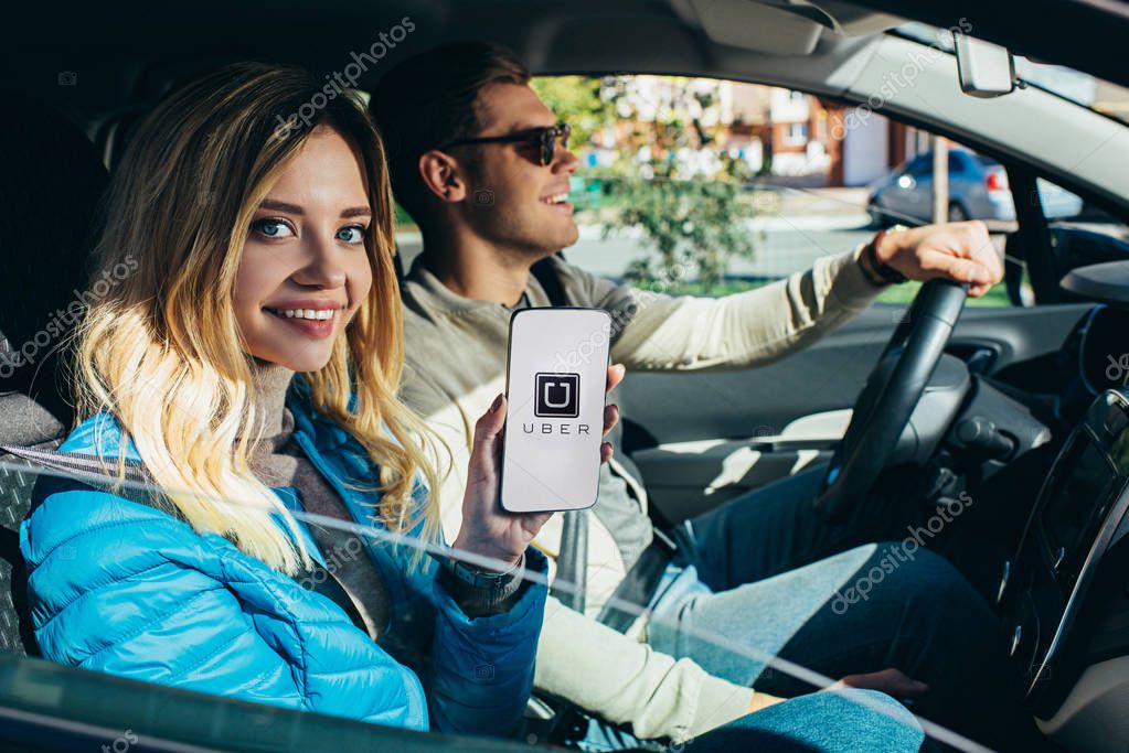 Smiling woman showing smartphone with uber logo on screen while husband driving car