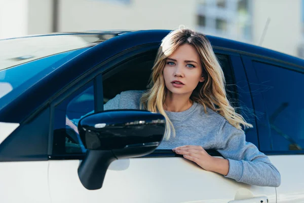 車を運転中にカメラを見て若い金髪女性の肖像画 — ストック写真