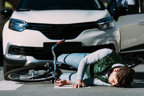 раненый молодой велосипедист лежит на дороге после ДТП
 