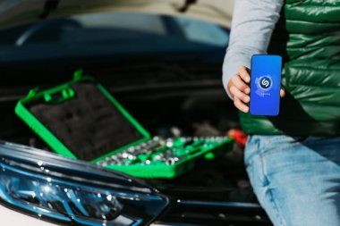 toolbox ile kırık araba üzerinde otururken smartphone shazam app ile tutan adamın kırpılmış atış