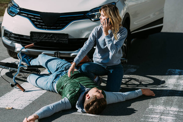 high angle view of woman calling emergency white injured cyclist lying on road after traffic collision 