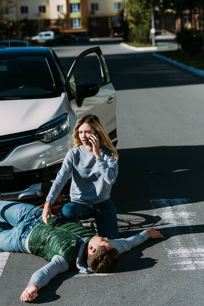 high angle view of young woman calling emergency white injured cyclist lying on road after car accident  