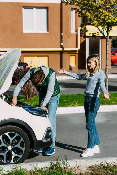 Emotionale Junge Frau Gestikuliert Und Schaut Mann Der Kaputtes Auto — kostenloses Stockfoto