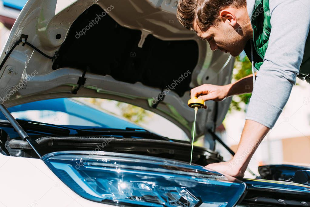 young man checking engine oil level in broken car