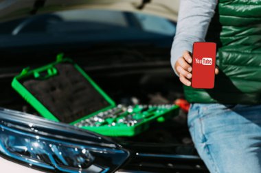 toolbox ile kırık araba üzerinde otururken smartphone youtube uygulaması ile tutan adamın kırpılmış atış