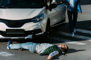 cropped shot of woman opening car door and going to injured man lying on road after car accident  clipart