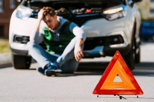 close-up view of road sign and upset man sitting near broken car on road
