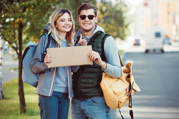 Happy Young Couple Backpacks Holding Blank Card Smiling Camera — Free Stock Photo