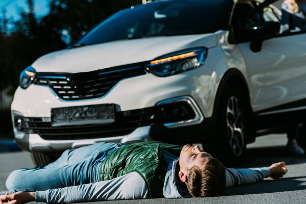 injured young man lying near car on road after traffic accident 