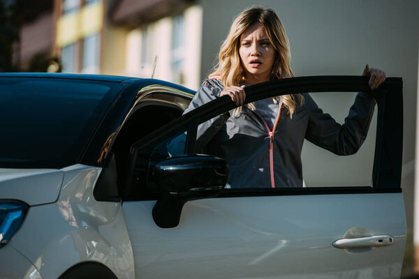 испуганная молодая женщина открывает дверь машины и смотрит в сторону после ДТП
