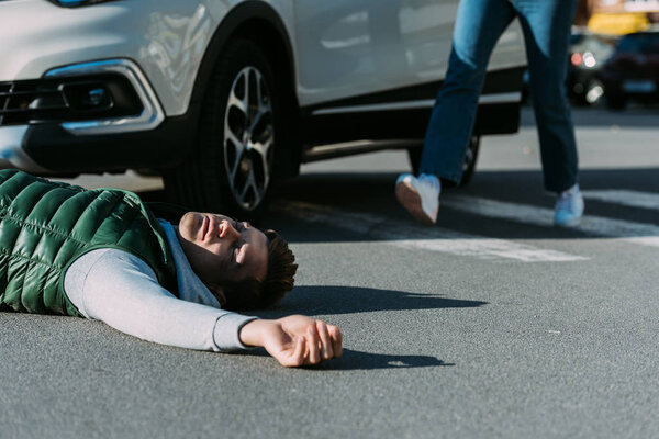 cropped shot of woman running to victim of car accident lying on road