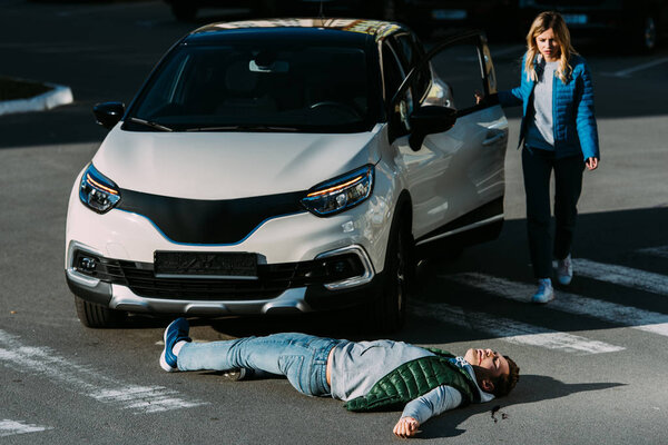 молодая женщина, открывающая дверь машины и идущая к раненому человеку, лежащему на дороге после автомобильной аварии
  