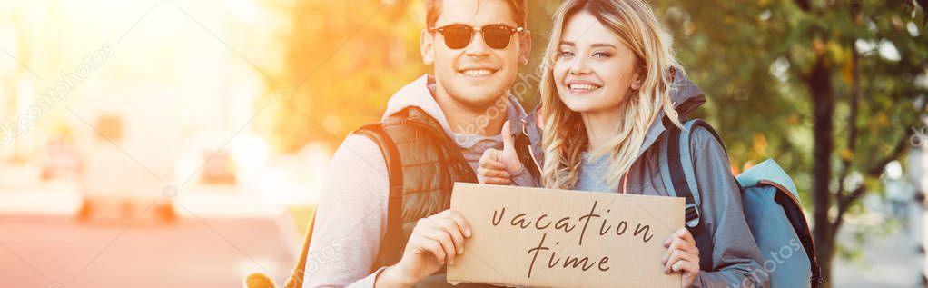 happy young couple of travelers holding card with inscription vacation time 