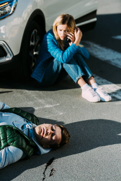 high angle view of scared young woman calling emergency while injured man lying on road after traffic collision 