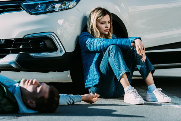 Mujer Joven Asustada Sentada Cerca Coche Hombre Herido Acostado Carretera — Foto de stock gratis