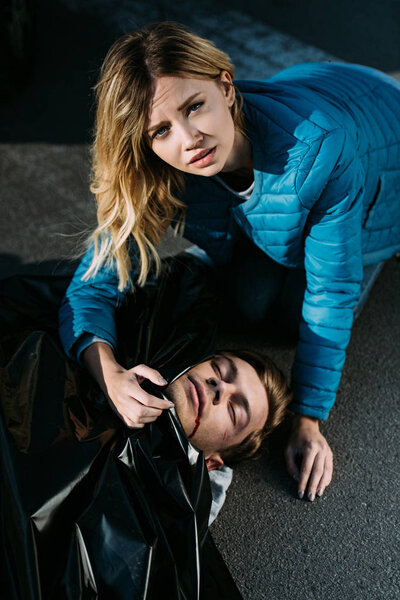 high angle view of young woman crying about dead body and looking at camera on road