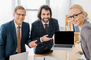 işçiler ile ayakta ve office içinde laptop gösteren genç gülümseyen erkek sigorta acentesi