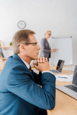 ofiste beyaz tahta gösteren tablo ve genç kadına oturan düşünceli yetişkin adam