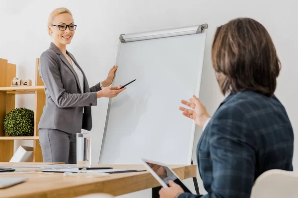 Unga Leende Kvinna Som Pekar Whiteboard Och Man Sitter Vid — Gratis stockfoto