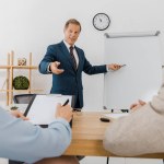 Businessman pointing at white board while couple signing contract on clipboard