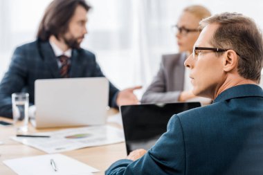 Toplantı sırasında dizüstü bilgisayarlar ile masada oturan ofis çalışanları 