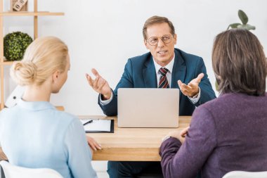 adult insurance agent in glasses talking to young couple in office clipart