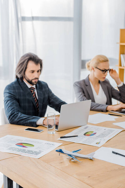 office workers using laptops with small toy airplane at wooden table in office