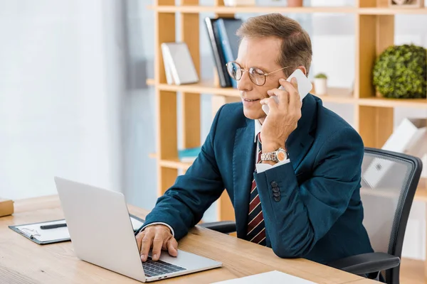 Adult Smiling Businessman Glasses Talking Smartphone Using Laptop Office — Stock Photo, Image