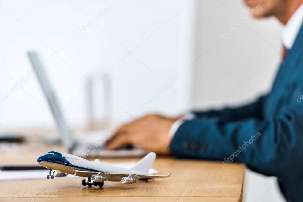 toy airplane at wooden table with office worker using laptop on blurred background 